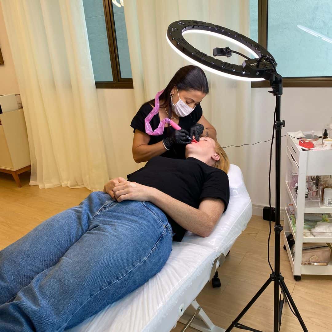 Profissional de beleza realizando procedimento estético em cliente deitada.